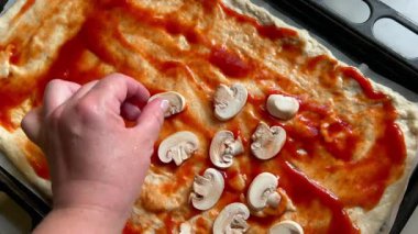 Şef domates soslu pizza hamuruna dilimlenmiş mantar ekliyor.