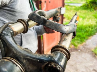 Hasarlı ve kirli bir bisiklet çatalını tutan tamircinin yakın çekimi.