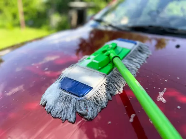 Araba temizleyicisi yaz boyunca kırmızı araba kaputunu özel paspas ve sabunla temizliyor.