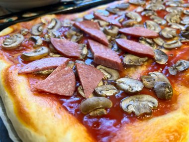 Domates soslu, dilimlenmiş pepperonili ve mantarlı çiğ ev yapımı pizza.