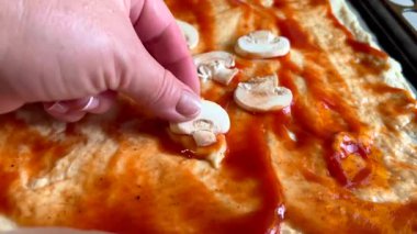 Şef domates soslu pizza hamuruna doğranmış mantar ekliyor.