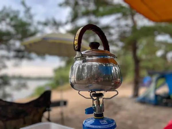 Yaz tatili boyunca kamp alanındaki taşınabilir gaz sobasında parlak metal çaydanlık kaynar su.