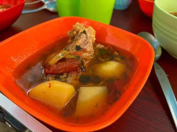 Canlı bir portakal kasesinde servis edilen dereotlu ve domatesli taze et ve patates çorbası, tadını çıkarmaya hazır.