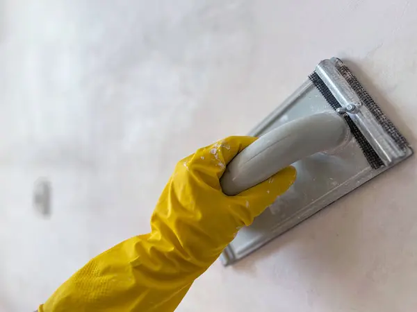 İnşaat işçisi duvarları zımparalamak için zımparalama aleti kullanıyor, ev yenileme sırasında boyama veya duvar kağıtları için yüzey hazırlıyor