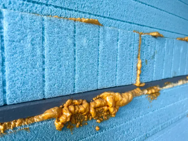 İnşaat sırasında mavi XP panoları arasında genişleyen köpük yalıtımının yakın plan görüntüsü