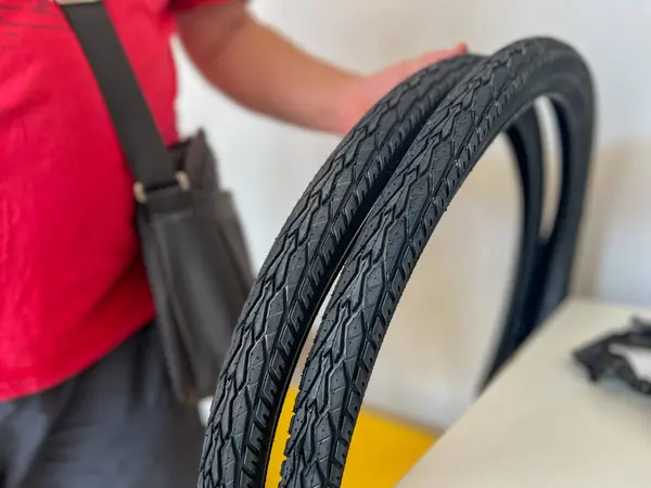 Bisiklet tamircisi atölyedeki yıpranmış tekerlekleri değiştirmek için iki yeni bisiklet lastiği gösteriyor