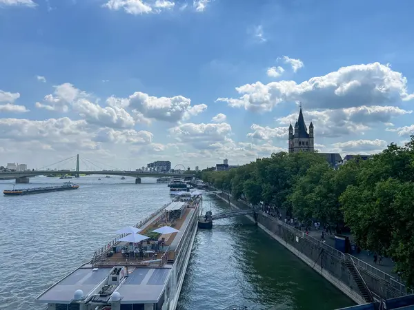 Parfüm şehri manzarası, nehir kenarı, hohenzollern köprüsü, büyük St. Martin kilisesi ve bulutlu bir gökyüzü olan güneşli bir günde demirlemiş nehir yolcu gemisi.