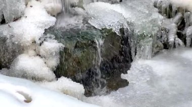 Small waterfall flowing between ice and snow in winter