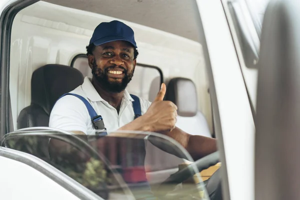 Portrait of courier black man in the truck thumb up and smiling to camera while sitting in driver seat, Optimistic man worker with delivery occupation.