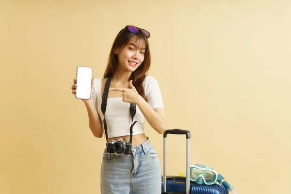 Asian woman traveler concept with luggage and camera holding smartphone which is showing blank white screen. Concept to present application on smartphone.