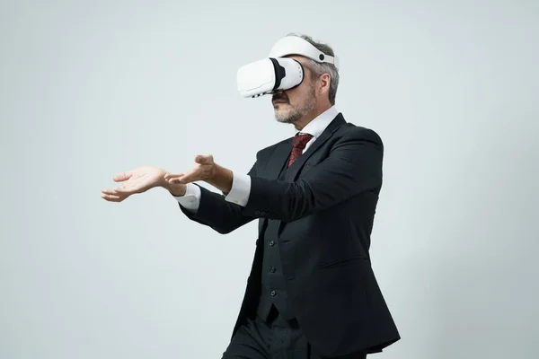 Virtual reality concept with senior businessman wearing VR glasses on his head raised his hand to show on the empty space.