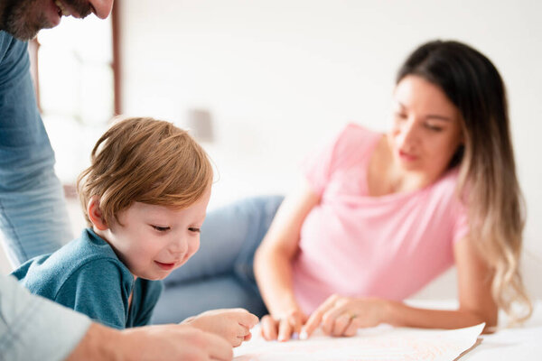 Happy family time, young toddler learning and having fun with parents enjoy relaxing day on bed, parenthood, self-esteem, happiness, quality time.