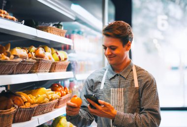 Marketteki taze meyve dükkanında gizli hayat tarzı genç bir adam raftaki ürünlerin kalitesini kontrol ediyor. Maskesiz genç bir erkek, mini sanatlarda çalışıyor..