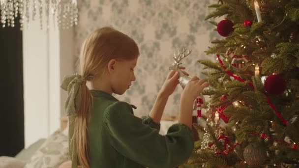 드레스를 아름다운 아가씨가 손님을 기다리며 크리스마스 트리를 장난감으로 장식한다 고품질 — 비디오