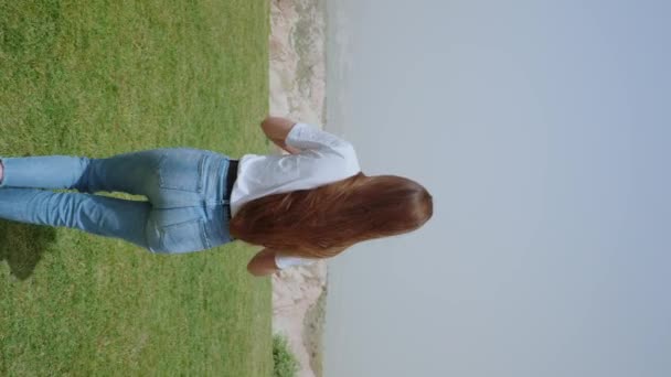 スローモーション バックビュー夏の昼間に靴なしで緑の芝生の上を歩く魅力的な女性 垂直ビデオ4K — ストック動画