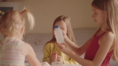 Çocuklar bir kimya deneyi yapmaya hazırlanıyorlar. Evde eğitim, çocuk gelişimi, tüm aile için hobiler. Üç kız masada oturup bileşenleri olan konteynırlara bakıyorlar..