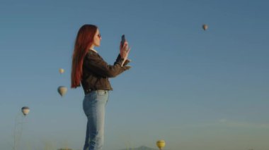 Kapadokya 'da sabah gökyüzünde yüzen sıcak hava balonlarının fotoğrafını çeken gezgin bir kadının yan görüntüsü