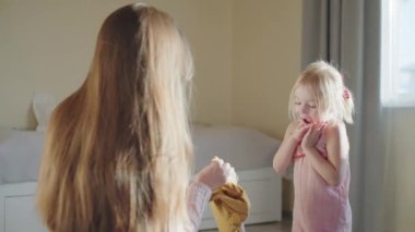 Anne, sarı elbiseli kızına paketini gösteriyor. Küçük kız, ağzı açık dururken güçlü, ışıl ışıl duygular yaşıyor. Aile hızlı teslimat kullanır, bir e-ticaret hizmeti kavramı.