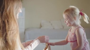 Genç anne kızına çevre dostu bir hediye veriyor. Heyecanlı kız hediyeyi kabul ediyor. Mutlu Çocukluk Konsepti, ebeveynlik, geri dönüşümlü kağıt, ekolojik trend, el işi kağıdı. 4k ağır çekim