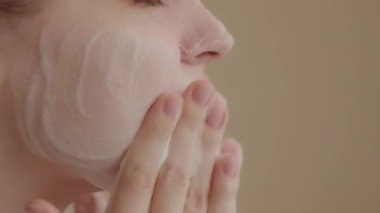 Young woman washes face with face wash foam. Daily facial skin care routine. Closeup view, slow motion 4K footage