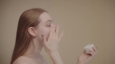 Side view beautiful young woman, applying face foundation or moisturizer, enjoying the process. Skin care, professional care product cosmetics advertisement concept. Slow motion shot. 4k footage