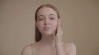 Funny happy attractive young woman applies skin care cream to her face, looks at the camera, applies moisturizing facelift cream, healthy skin care concept. 4k footage