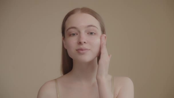 面白い幸せな魅力的な若い女性は彼女の顔にスキンケアクリームを適用し カメラを見て 保湿フェイスリフトクリーム 健康的なスキンケアコンセプトを適用します 4K映像 — ストック動画