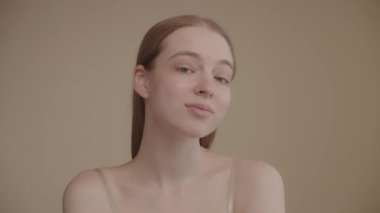 Head shot Young woman of Caucasian ethnicity Healthy blonde woman with blue eyes looks into the camera, enjoying the condition of her skin, slow motion. Beauty and skin care concept. 4K