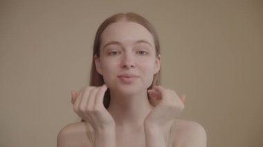 Young lady with blue eyes applies serum to her face, looking into the camera, isolated against a light background Beautiful model girl with perfect clean skin Concept of a skincare or cosmetics ads 4k