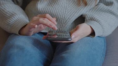 Kadın parmak, telefon ekranı kaydırma kaydırmasına dokunur. Sosyal ağları taramak, pazar yerinde ürünleri aramak, çevrimiçi mağazada ürünleri seçmek. Kanepede oturan genç bir kadın akıllı telefon kullanıyor.