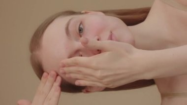 Head shot Confident attractive young lady looks into the camera and applies moisturizing toner to face with proper hand movements. face massage, facial fitness, skincare concept ads. Slow motion 4k