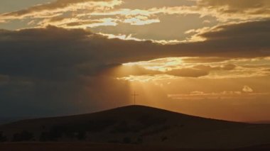 Cross on hill Sun rays slowly appear from behind clouds Silhouette Cross against the background of sunset light in the rays sun Victory of Light over darkness Death and Resurrection of Jesus Christ