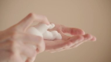 Aşırı yakın çekim, izole edilmiş arka planda eller, yüzü, cilt bakımını, temizliği, hijyeni, sağlık hizmetlerini yıkamak için köpük veya köpük uygulayan genç bir kadın. Şişeden köpük alan parmak baskıları Yavaş çekim
