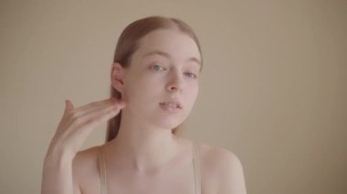 Genç, sağlıklı, sakin bir bayan kameraya bakar, pürüzsüz cilt bakımına dokunur, cilt bakımı kavramı. Cilt bakım ürünleri, sivilce önleyici ürünler, serum, cilt temizleyici, nemlendirici, yüz gerdirme. Yavaş çekim