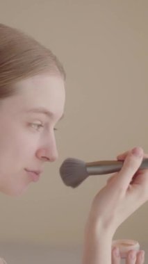 Mutlu genç kadın yüzüne pudra sürüyor, sağlıklı cilt fırçası, gülümseyen güzel kız Z jenerasyonu makyaj yapıyor aynada aynaya bakıyor sabah güzelliği rutin videosu