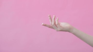 Kadın model, işaret parmağına bir damla nemlendirici damlatarak elini kaldırıyor. Nemlendirici reklamı konsepti. Pembe arkaplan Güzellik Koleksiyonu