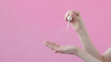 Süper yavaş çekim, kadın eli damlatıcı, yüz serumu, avuç içine damlayan serum. Cilt bakımı, güzellik kremleri, yaşlanma karşıtı, kaldırma, sivilce önleyici. Pembe arkaplan Güzellik Koleksiyonu