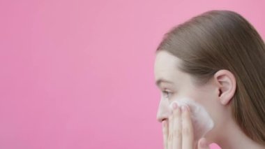 Ağır çekimde genç bayan yüz temizleme köpüğü sürüyor. El hareketleri, Temizleyici Yanak Burun Stüdyosu çekimi. Sivilcelerle mücadele, güzellik rutin kişisel bakım konsepti. Pembe arkaplan Güzellik Koleksiyonu