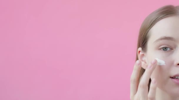若いブロンドの女性は頬に保湿剤を適用します 顔のスキンケアの概念 ピンクの背景美容コレクション — ストック動画