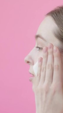 Genç bayan yüzünü köpükle yıkar. Dikey video, pembe arka plan. El hareketleri Yanakları Temizleme Stüdyosu çekimi. Sivilce önleyici reklam konsepti cilt bakım rutini. Pembe arkaplan Güzellik Koleksiyonu 