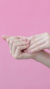 Kadın el bakımı. Eller yakın çekim, nemlendirici el kremi sürülüyor. Vücut bakımı reklamı konsepti. Pembe arka plan güzellik koleksiyonu. Dikey video.