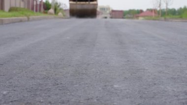 Yeni yol yüzeyi, ön planda yol kaldırımı arka planda bulanık asfalt kaldırım makinesi. Şirketlerin yol tamiri konsepti, yol bakımı. Yavaş çekim