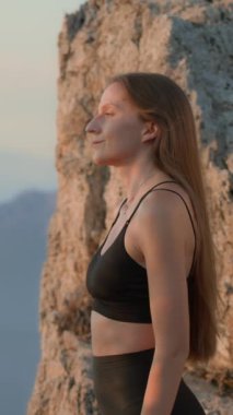 Boyun egzersizleri. Genç bir kadın, atletik kıyafetler, güzel manzaralı bir tepede duruyor, güneş doğuyor, boynunu ısıtıyor. Sağlıklı Yaşam Tarzı, Fitness, Refah ve Farkındalık Konsepti. Dikey video