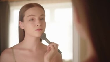 Yansımanın yakın çekimi genç sarışın kadın pudra sürüyor, sağlıklı cilt fırçası, sakin güzel kız Z nesli sabah makyaj yapıyor, günlük güzellik rutini uyguluyor.. 