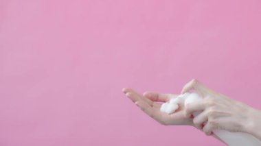 Aşırı yakın plan, elleri pembe arka planda, cilt temizleme hijyen hizmetleri için el köpüğü sabunu ya da köpük uygulayan genç bir kadın. Şişeden köpük alan parmak baskıları Yavaş çekim