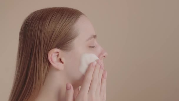 ヘッドショット若い女性は 顔の洗顔フォームサイドビューを置く 毎日のフェイシャルスキンケアルーチン リアルタイム映像 スタジオショット — ストック動画