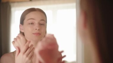 Mutlu genç bir kadın aynanın önünde dans ediyor, gülümseme el kremi sürüyor. Vücut bakımı konsepti, deri ellerini nemlendirmek.. 