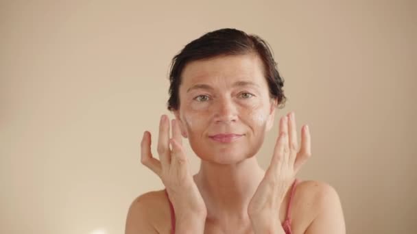 成熟女性使用保湿霜恢复皮肤弹性 一位50多岁的妇女的美丽肖像 宣传抗老化的面部整容产品 护理紧致的皮肤 隔离的背景 — 图库视频影像