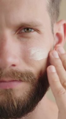 Aşırı yakın plan, yarım yüz ciddi özgüvenli genç 30 'lu yaşlarda, yüz nemlendirici sürüyor. Erkekler için yüz bakım ürünlerinin reklamı. İzolasyon arka planı, kopyalama alanı. Dikey görüntüler