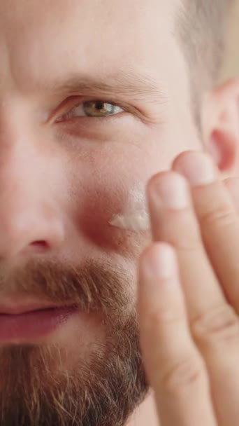 極端なクローズアップ 自信を持った30代の若者の半分顔 顔の保湿剤を適用します 男性用フェイシャルケア製品の広告 アイソレーションの背景 スローモーション コピースペース バーティカル映像 — ストック動画